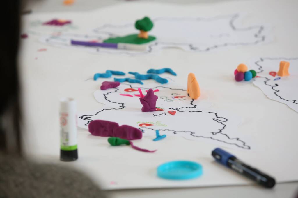 Creatures, plants and animals made from colourful play dough sit on a drawn map with different locations markers
