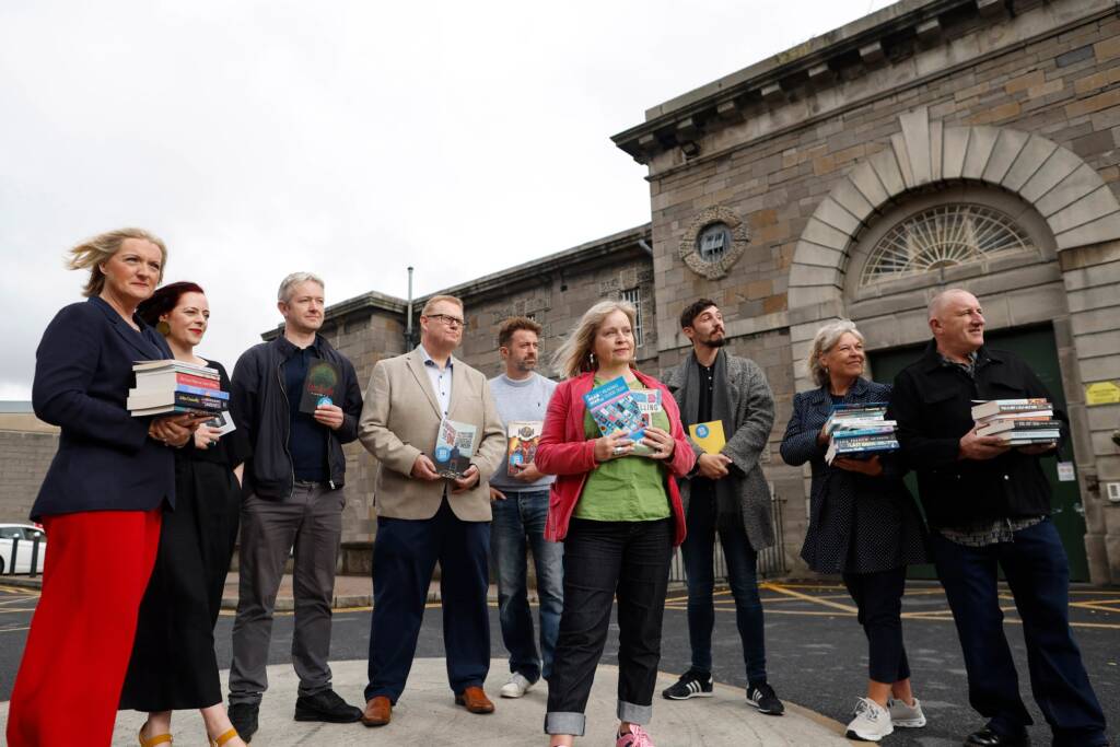 Writers and Irish Prison Service staff members stand outside Mountjoy Prison. They all hold books and look away from the camera.