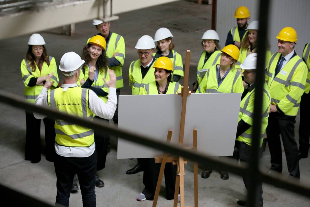 Minister Catherine Martin along with members of the Arts Council staff standin hard hats and reflective jackets as Grafton architects present at Dublin Port.