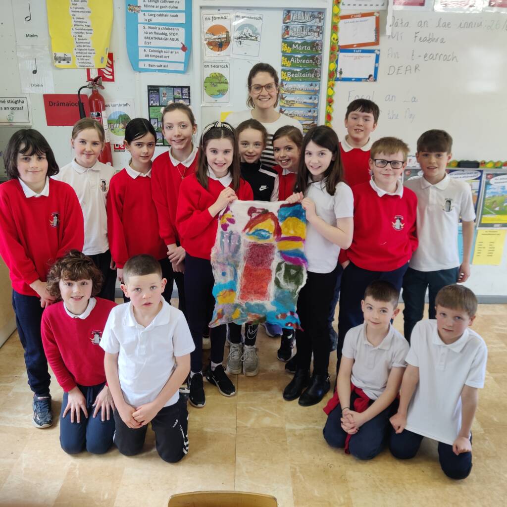 a group of students in red uniforms stand with their teacher holding up an artwork