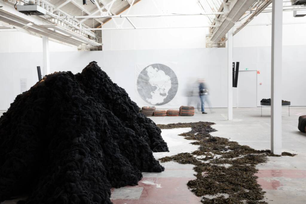 Installation image of 'In Search of Hy-Brasil'. Showing piles of ecological materials sitting on the floor of a white gallery space.