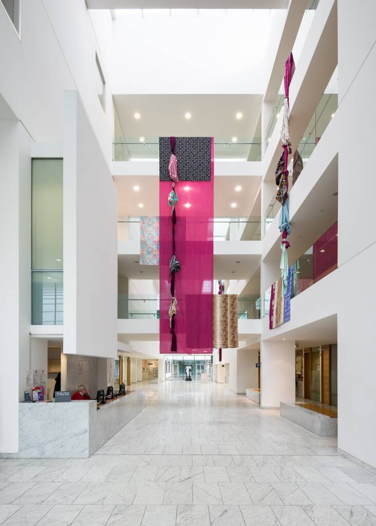 lengths of patterned material knotted together hangs over white balconys surrounded by other unknotted materials.