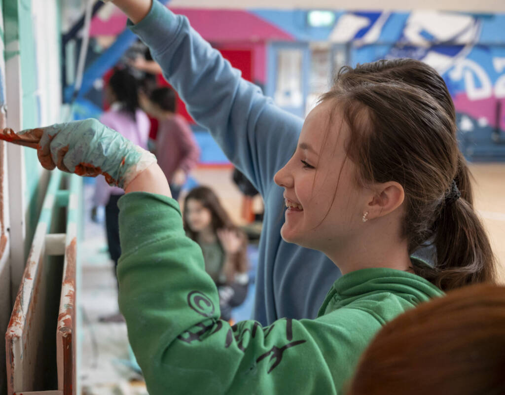 Close up of a young student painting a wall in a school hall